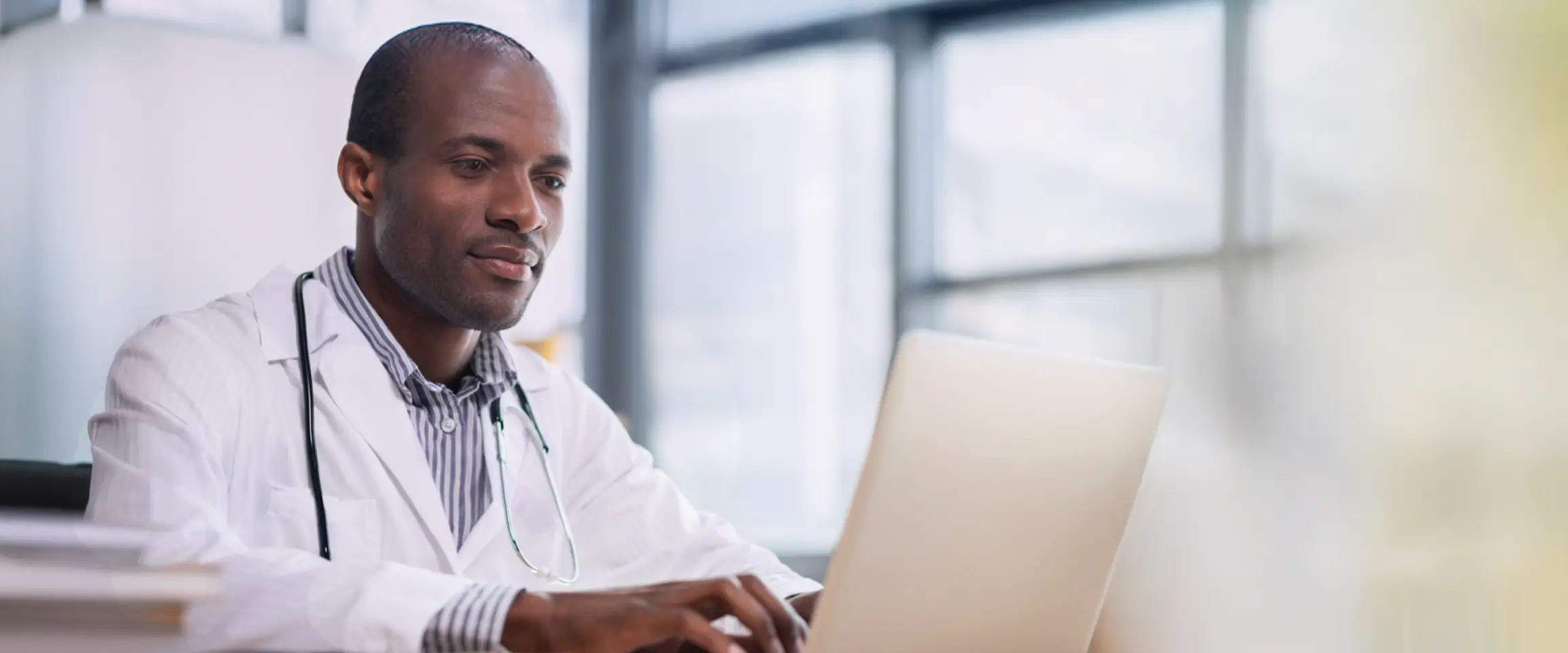 Healthcare professional sitting at desk typing on a computer. Actor portrayal.