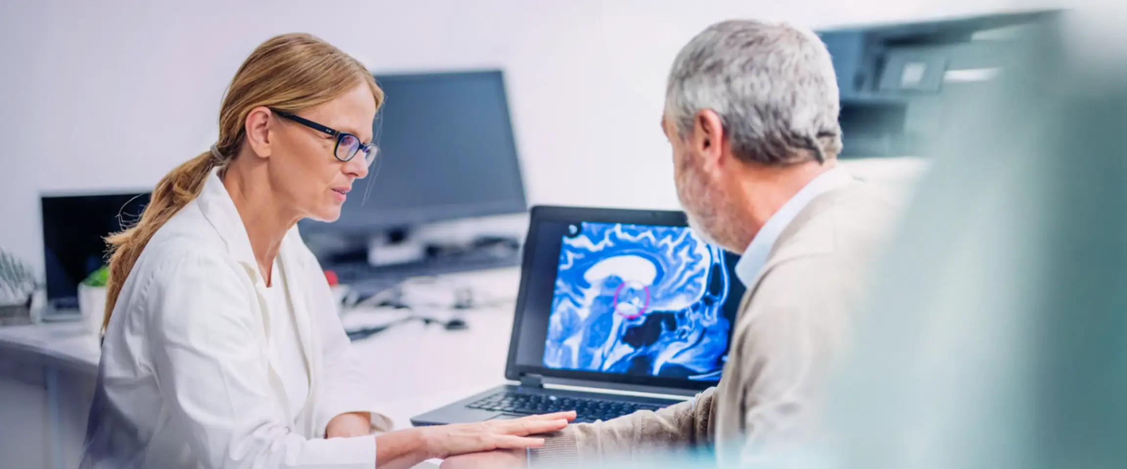 A man sitting with a healthcare professional, while they look at brain imaging on a monitor. Actor portrayals.
