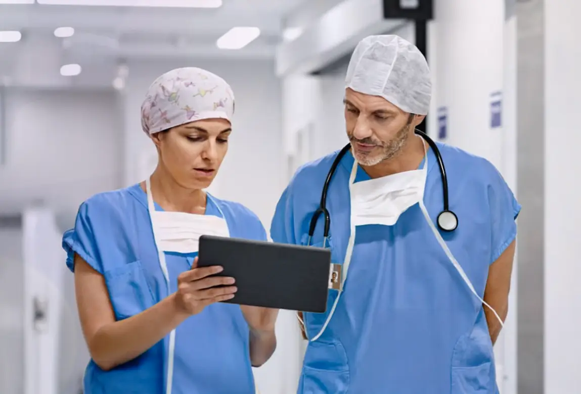 Two healthcare professionals, wearing scrubs, looking at information on a clipboard. Actor portrayals.