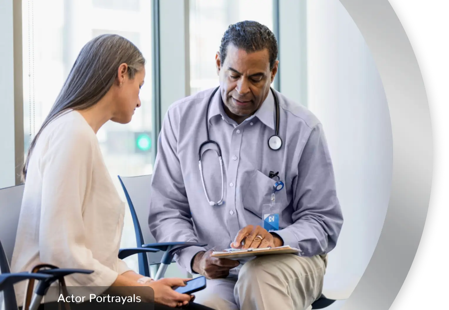 A woman sitting with a healthcare professional, while they look at a clipboard together. Actor portrayals