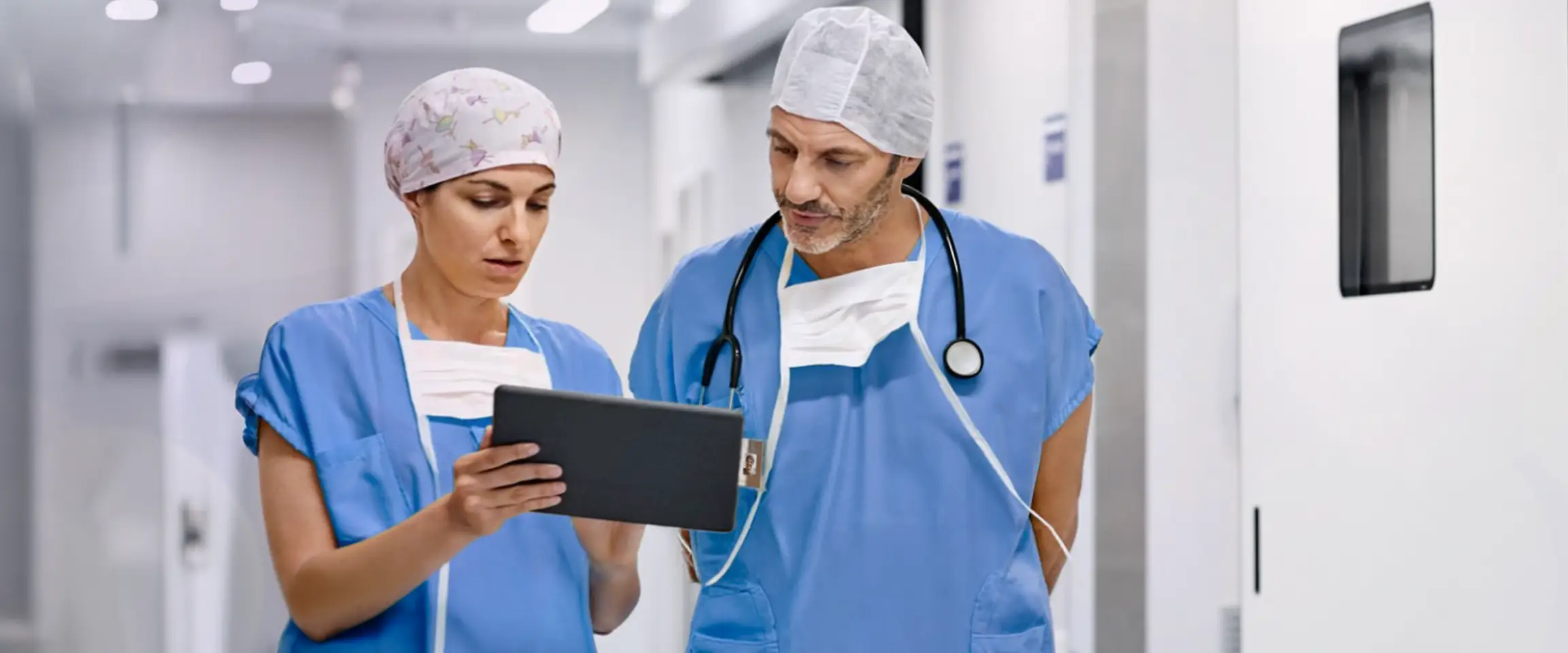 Two healthcare professionals, wearing scrubs, looking at information on a clipboard. Actor portrayals.