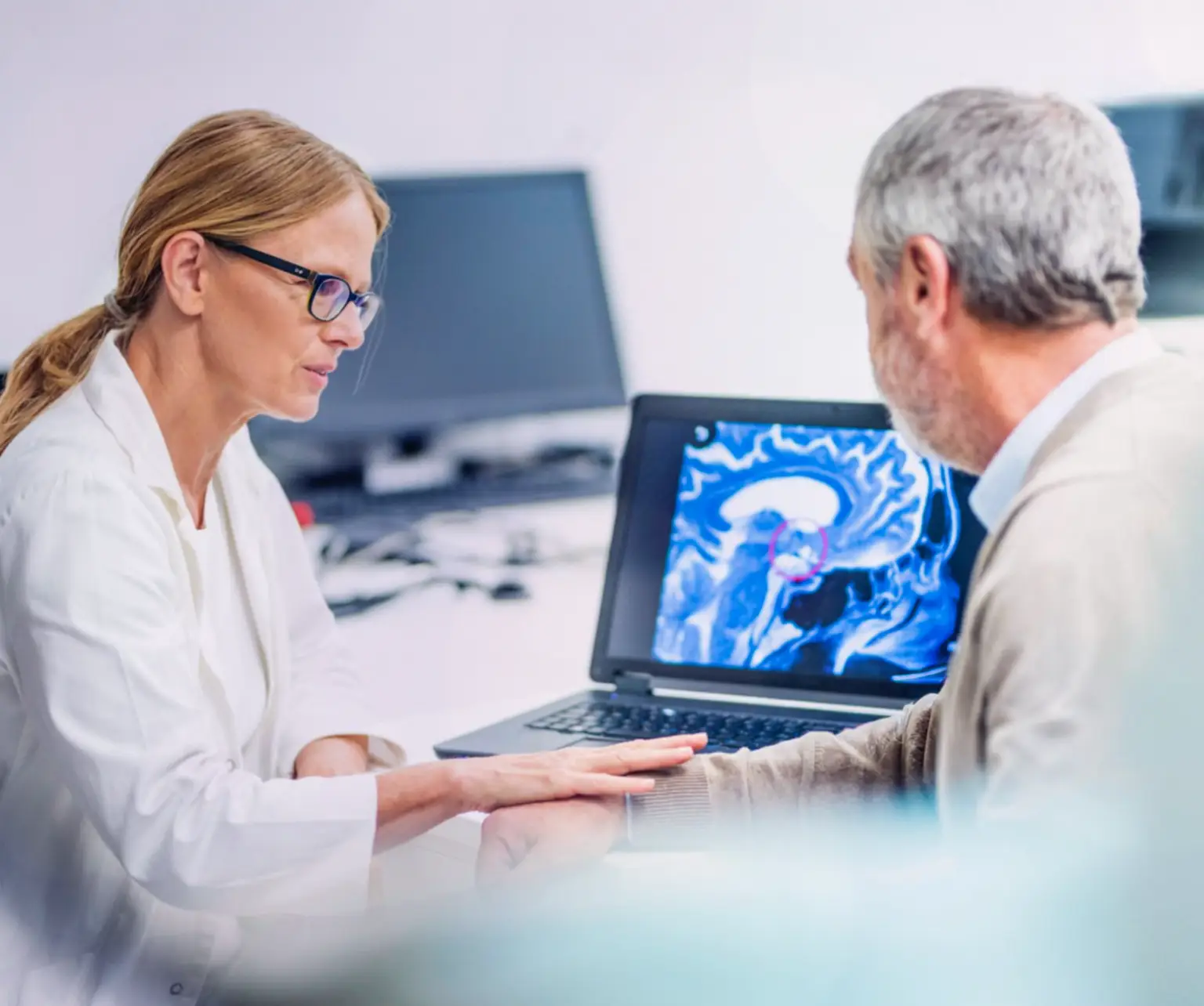 A man sitting with a healthcare professional, while they look at brain imaging on a monitor. Actor portrayals.
