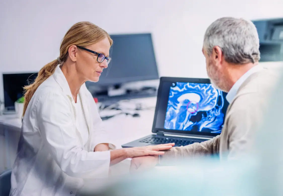 A man sitting with a healthcare professional, while they look at brain imaging on a monitor. Actor portrayals.