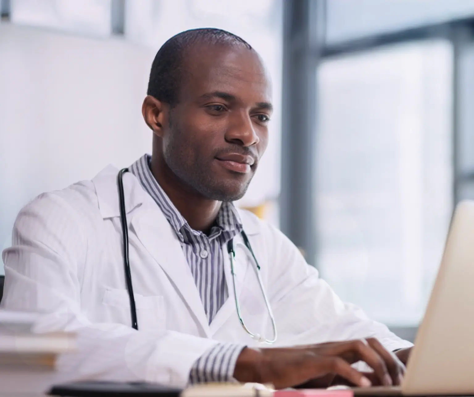Healthcare professional sitting at desk typing on a computer. Actor portrayal.