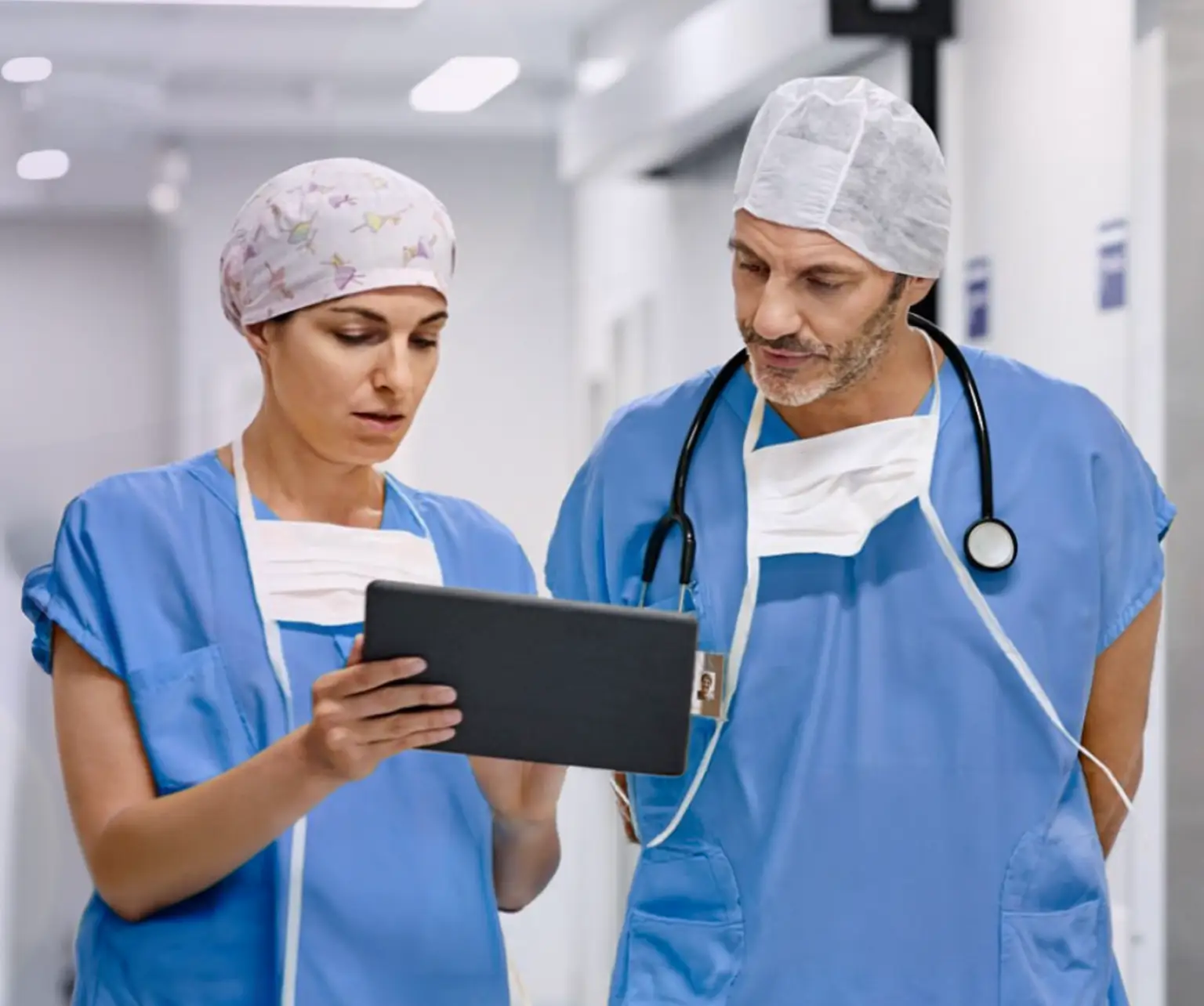 Two healthcare professionals, wearing scrubs, looking at information on a clipboard. Actor portrayals.