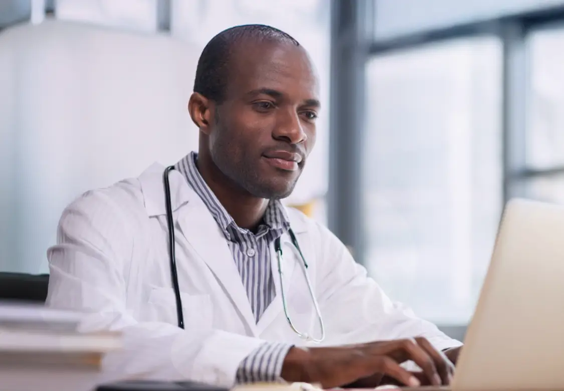Healthcare professional sitting at desk typing on a computer. Actor portrayal.