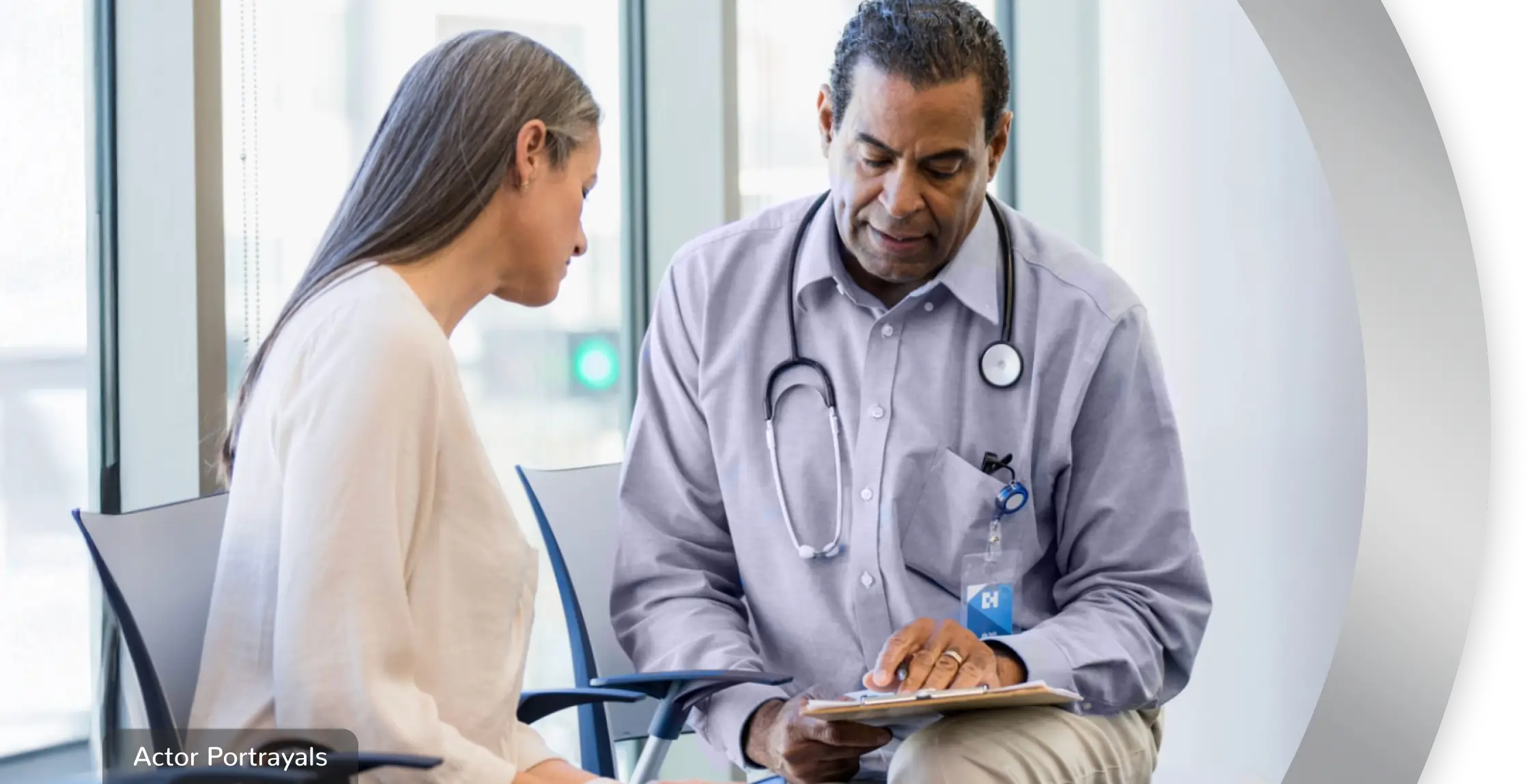 A woman sitting with a healthcare professional, while they look at a clipboard together. Actor portrayals